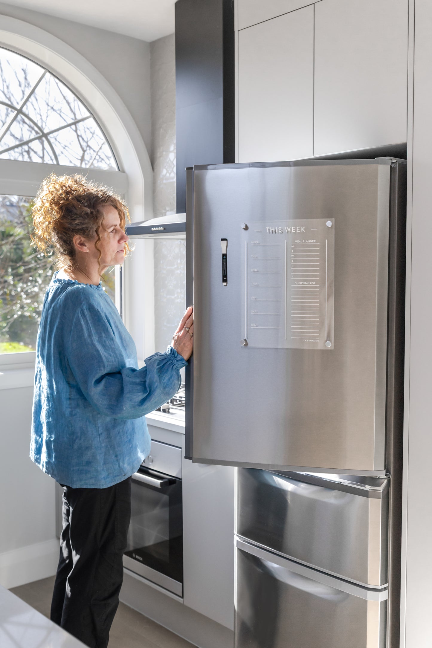 Person interacting with a stainless steel refrigerator and meal planner in a modern kitchen.