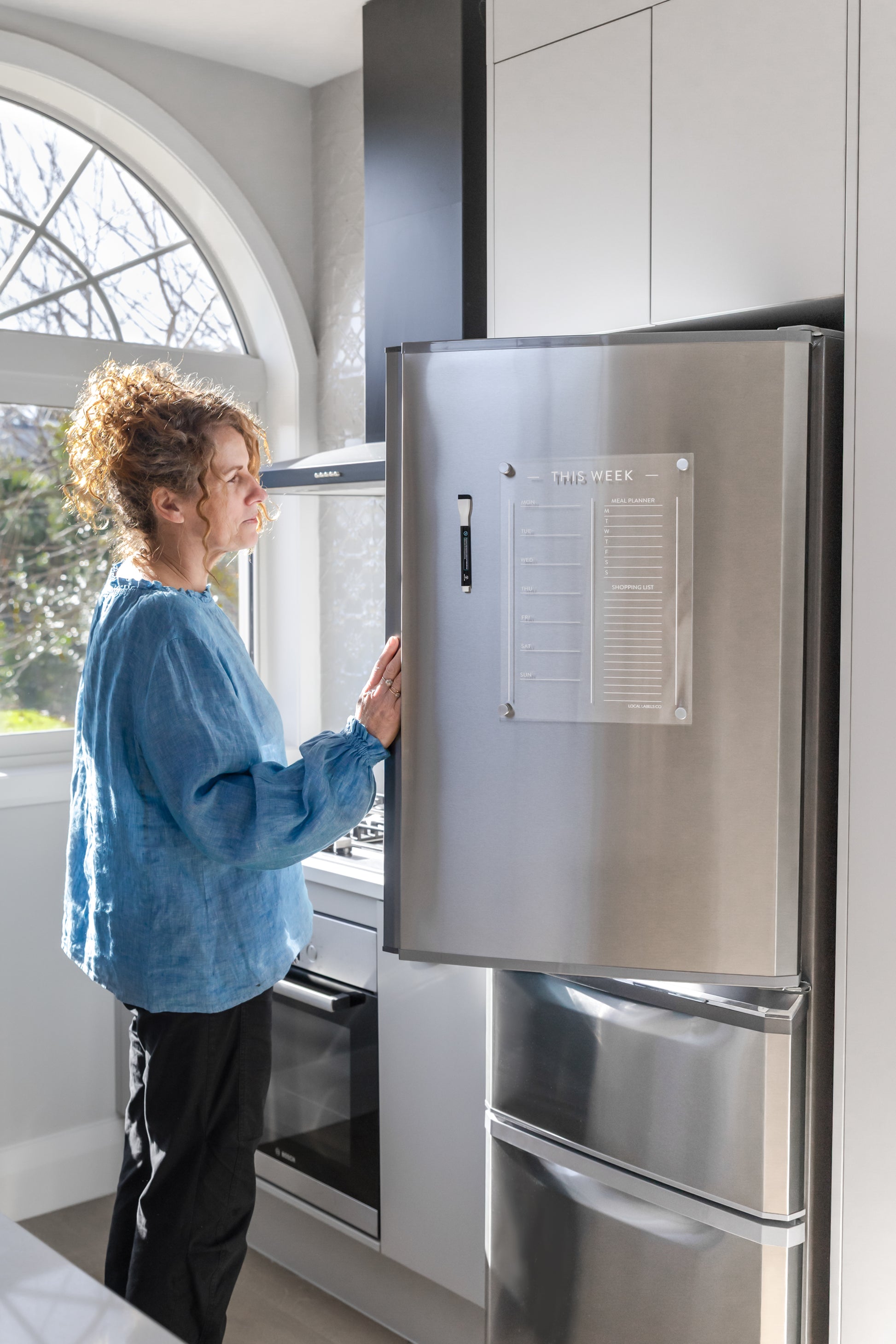 Person interacting with a stainless steel refrigerator and meal planner in a modern kitchen.