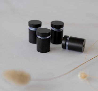 Matte black stainless steel standoff brackets with rubber bumpers, designed to securely mount and elevate acrylic planners off the wall, creating a modern floating display.