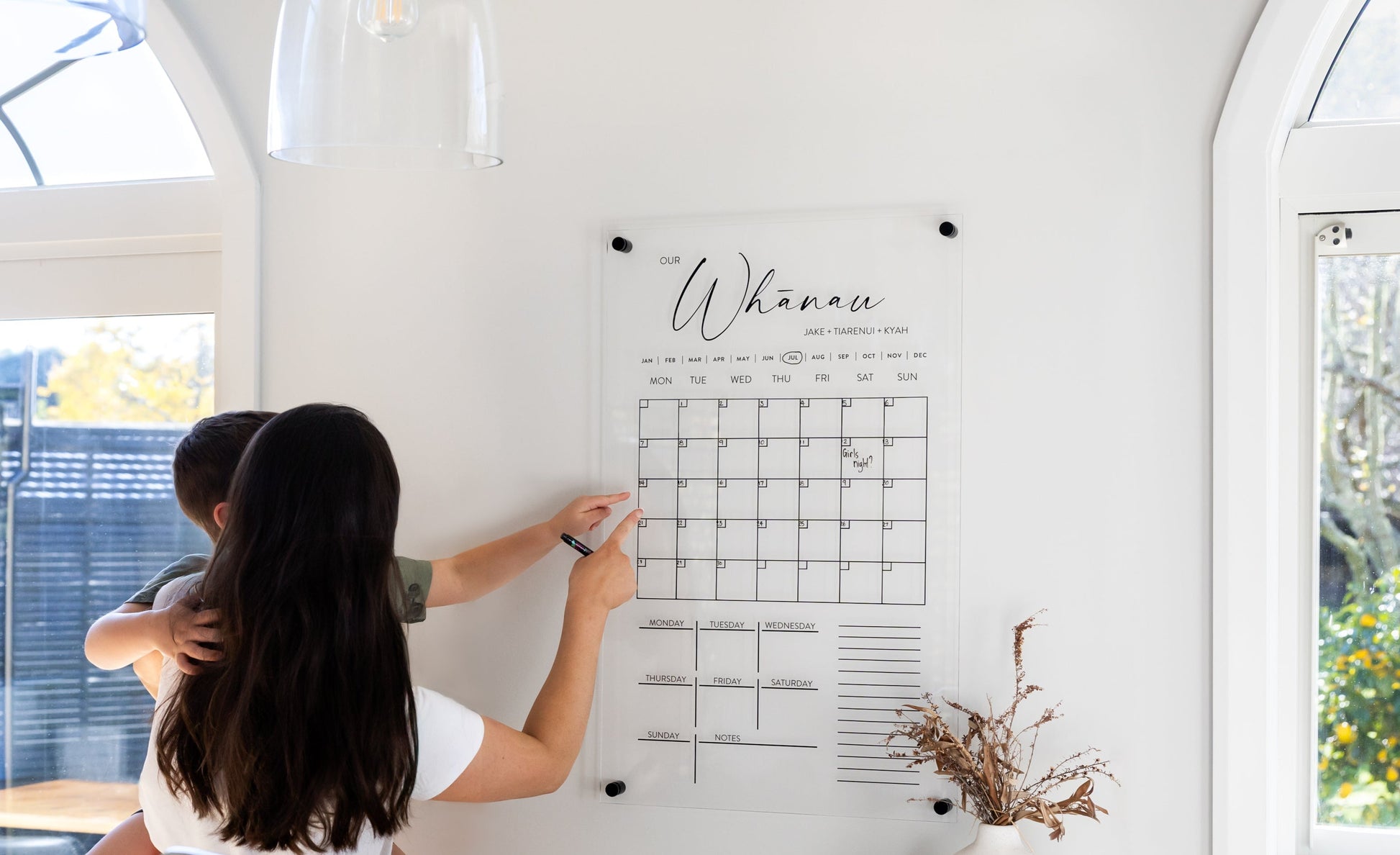 Mother and child using acrylic wall calendar together, family planning on modern frameless calendar