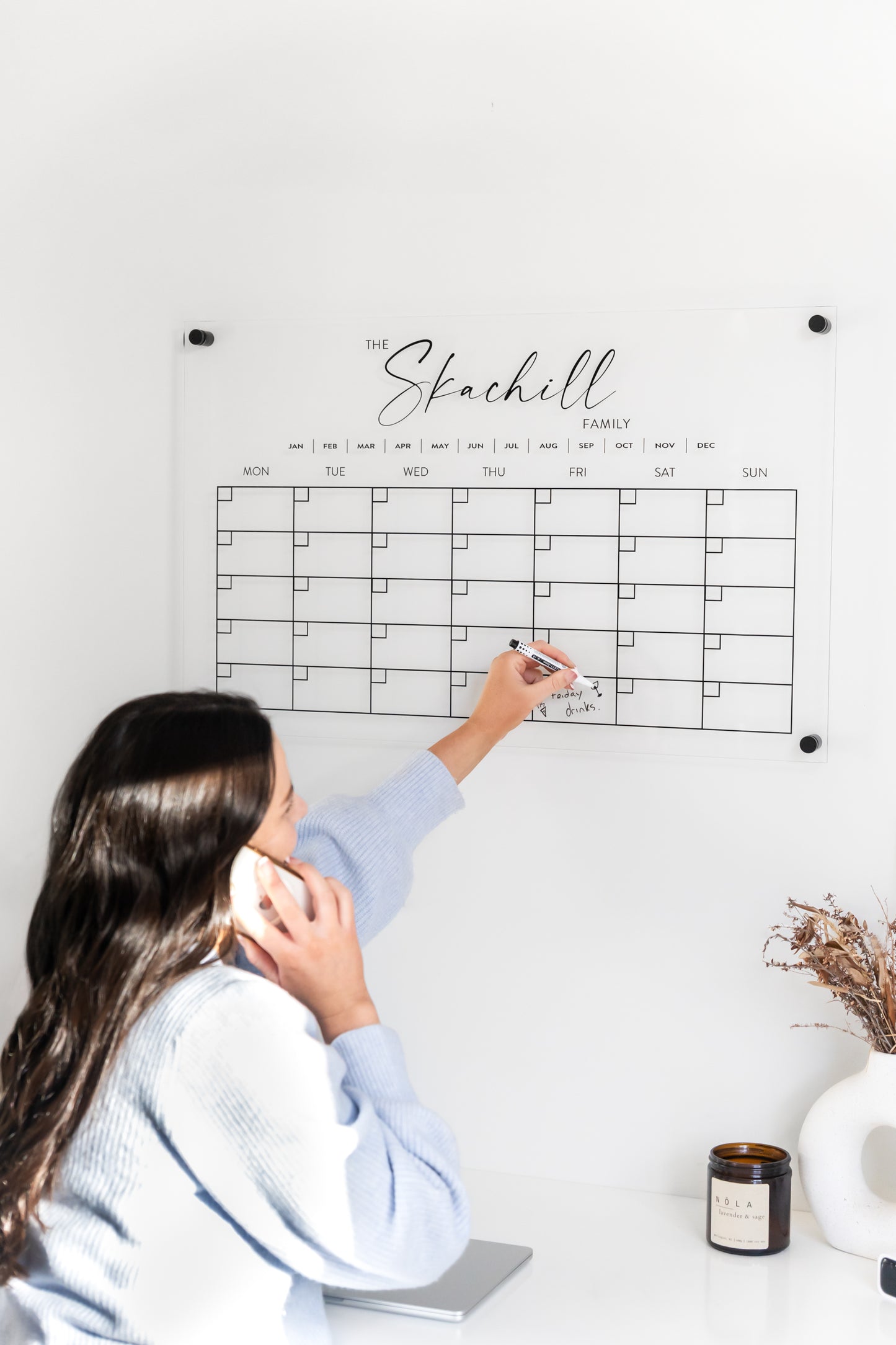 Woman using a large personalised monthly acrylic wall calendar in a home, featuring elevated standoff brackets and feminine design.
