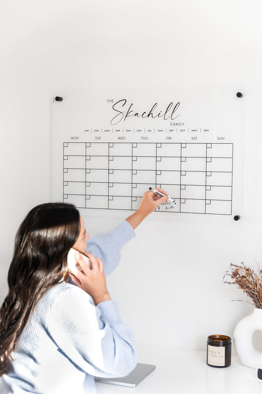 Woman using a large personalised monthly acrylic wall calendar in a home, featuring elevated standoff brackets and feminine design.